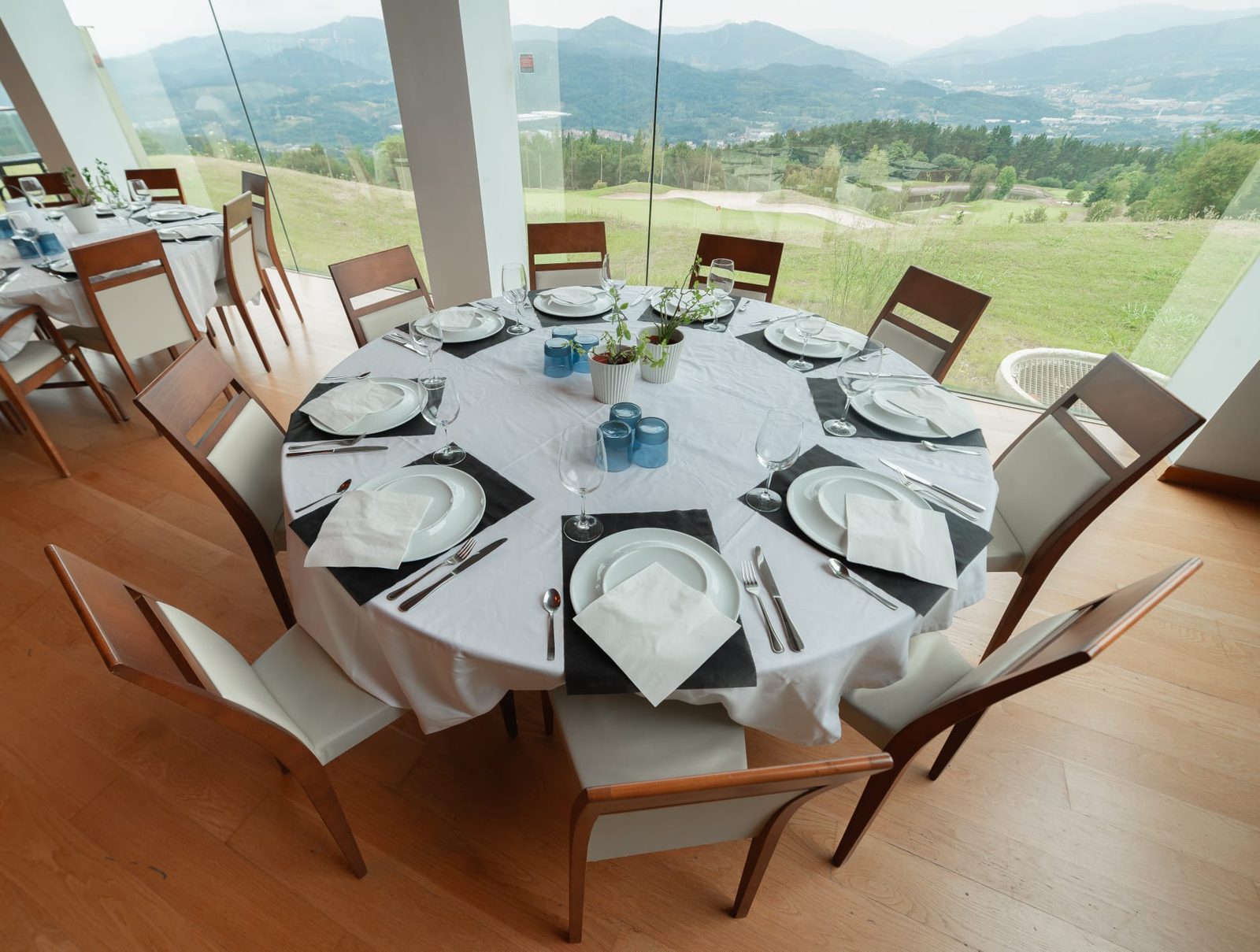 Mesa redonda preparada junto al ventanal, con el campo de golf y los Montes de Vizcaya al fondo